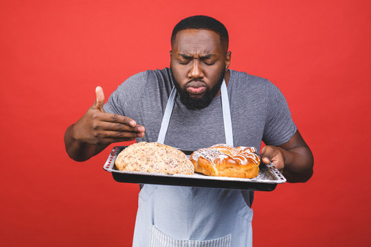 Crazy young african american male chef cook or baker man in striped apron grey t-shirt posing isolated over red background. Cooking food concept. Mock up copy space.