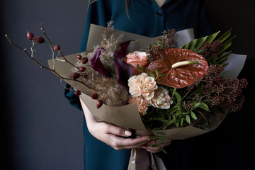 Female hands holding a bouquet decorated in vintage style on a dark background, selective focus