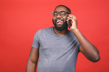 Portrait of a happy african american guy talking on mobile phone isolated against red background.