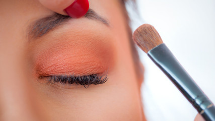 Makeup professional artist applying base color eyeshadow on model eye - obrazy, fototapety, plakaty