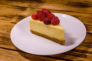 White plate with cheesecake New York and raspberries on wooden table