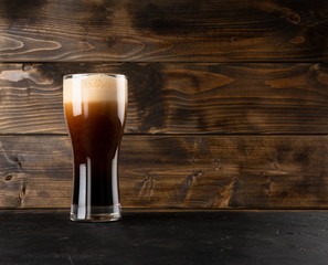 Dark beer in glass on black table and wooden wall background