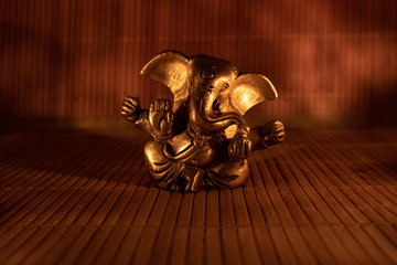 Isolated golden ganesha figure on wooden mat illuminated by candlelight, close up