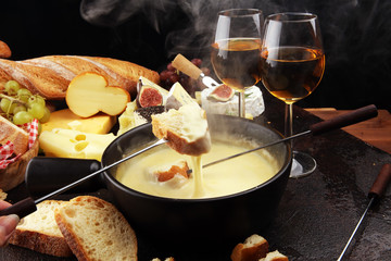 Wyśmienity szwajcarski obiad fondue w zimowy wieczór z różnymi serami na desce obok podgrzewanego garnka serowego fondue z dwoma zanurzonymi widelcami - 300464268
