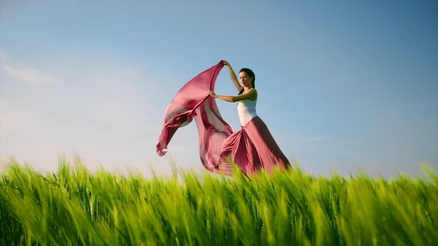 Classic dance on field background. Professional female modern dancer in pink fabric dress dancing in green grass.