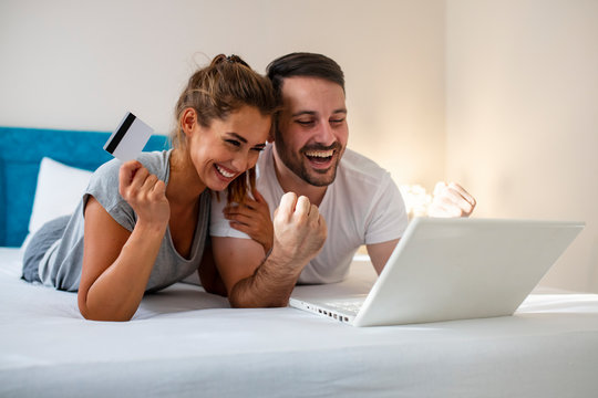 Happy couple buying online, using laptop and credit card in bed, enjoying shopping in internet, free space. Happy couple shopping online in a hotel room. Happy couple using laptop on bed at home