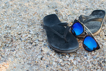 Fototapeta na wymiar Sunglasses and black rubber beach slippers on the beach. Vacation at sea. Beach accessories, protection. Flip Flops. Reflections of the sky in sunglasses. Summer season, hot season. Place for text.