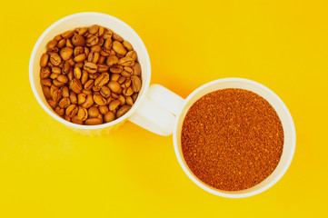 Coffee beans and ground coffee in cups on yellow background