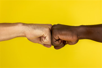 central view of  european and afroamerican hand to hand clenched into fists on the yellow background