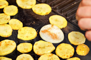 Slices potatoes and onion seasoned with spice grilled on electric grill, closeup photo