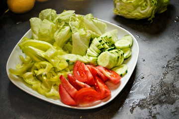 Cut tomatoes, cucumber and iceberg salad on dark kitchen board