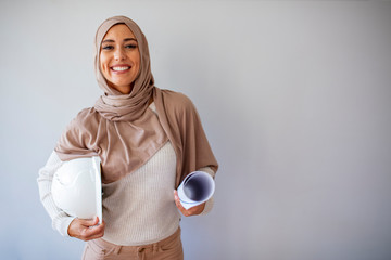 Young Muslim woman wearing a protective helmet standing on gray background. Portrait of a young...