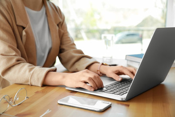 Young businesswoman using laptop at table in office, closeup