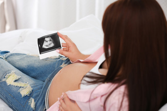 Pregnant woman with ultrasound picture on bed, closeup