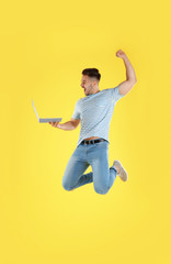 Fototapeta na wymiar Emotional man with laptop jumping on yellow background