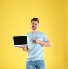 Happy man with laptop on yellow background. Space for text