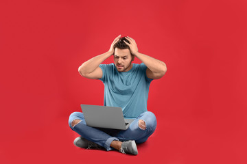 Emotional man with laptop on red background