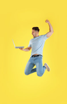 Emotional Man With Laptop Jumping On Yellow Background