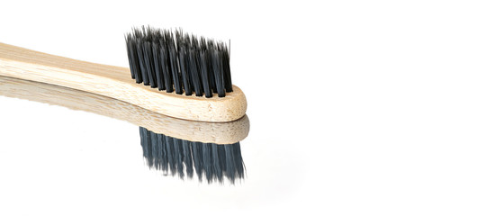 Wooden bamboo toothbrush with black bristles, closeup detail isolated on glossy white table reflection visible , space for text right side