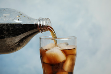 Pouring refreshing soda drink into glass on blue background, closeup