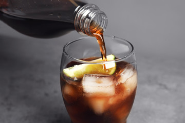 Pouring refreshing soda drink into glass on table, closeup