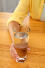 Woman holding glass of water at wooden table, closeup. Refreshing drink