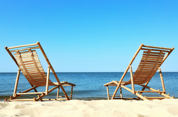 Sandy beach with empty wooden sunbeds on sunny day