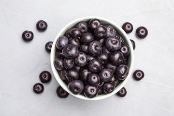 Bowl of fresh acai berries on light stone table, top view. Space for text