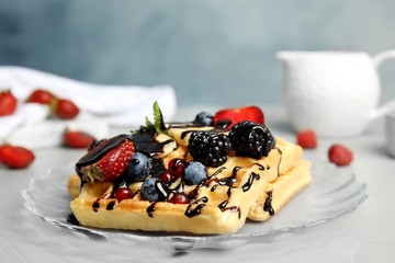 Delicious waffles with fresh berries served on table against blue background