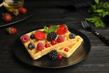 Delicious waffles with fresh berries served on black wooden table