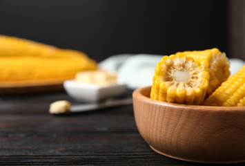 Wooden bowl of boiled corn cobs on black table, closeup. Space for text
