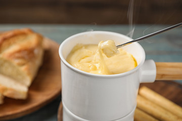 Pot of tasty cheese fondue and fork with bread on blue wooden table
