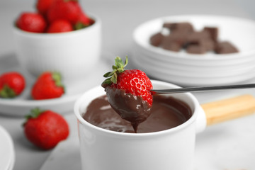 Dipping strawberry into fondue pot with chocolate on grey table, closeup