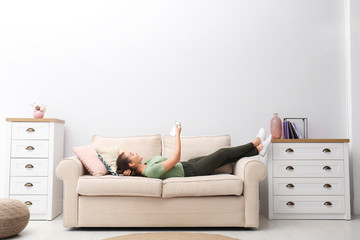 Happy young woman switching on air conditioner with remote control at home