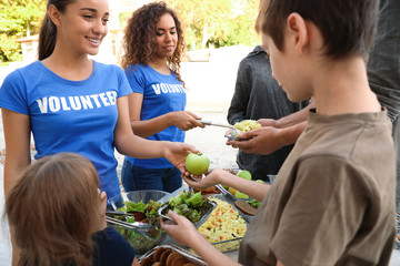 Volunteers serving food to poor people outdoors