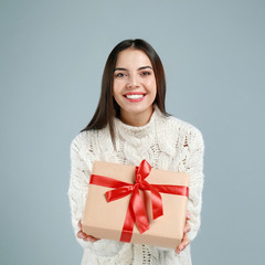 Fototapeta premium Happy young woman with Christmas gift on grey background