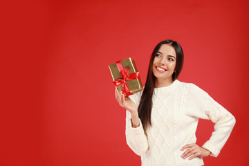 Happy young woman with Christmas gift on red background. Space for text