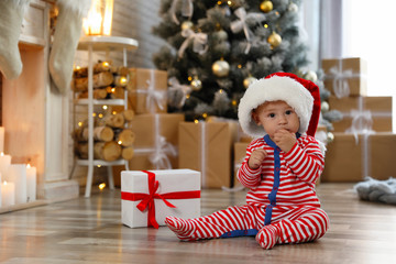 Fototapeta na wymiar Little baby with Santa hat and Christmas gift on floor at home