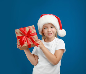Cute little child wearing Santa hat with Christmas gift on blue background