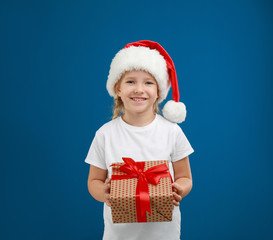 Cute little child wearing Santa hat with Christmas gift on blue background