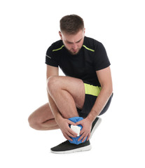 Young man with cold compress suffering from ankle pain on white background