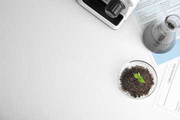 Petri dish with soil and sprouted plant on white table, flat lay. Biological chemistry