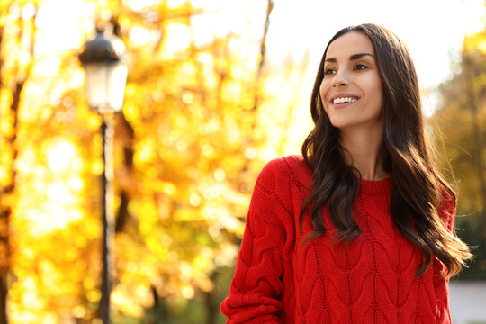 Beautiful woman wearing red sweater in sunny park. Autumn walk