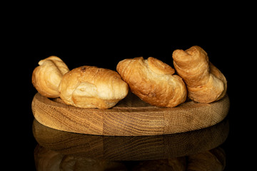Group of four whole fresh baked mini croissant on bamboo plate isolated on black glass