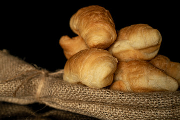 Group of six whole fresh baked mini croissant closeup with jute bag isolated on black glass
