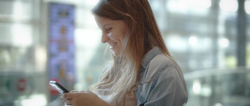 Woman with long hair and denim shirt smiling while texting on the cellphone, slow motion cinematic footage. BMPCC 4K