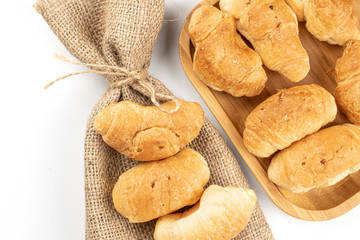 Lot of whole fresh baked mini croissant with jute bag on wooden square plate flatlay isolated on white background