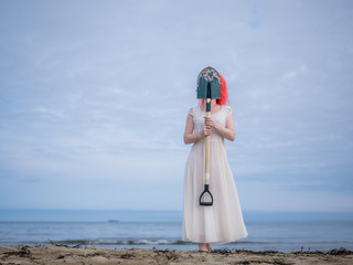 A girl in a white dress with a shovel covers her face