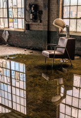 A room flooded with rain water with reflections of windows and an old hair dryer mounted to a chair. Image taken at the old Scranton Lace Factory, built in 1890, closed in 2002, demolished in 2019.
