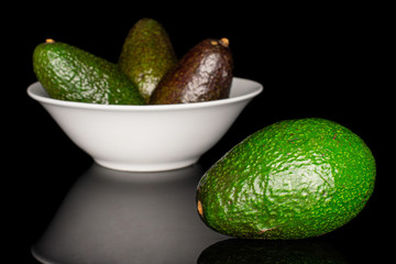 Group of four whole fresh green avocado in white ceramic bowl isolated on black glass